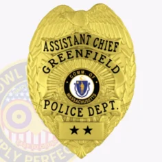 Riverbend police assistant chief’s gold metal badge with eagle figure at the top, clear black text including "assistant chief" and "greenfield police dept. ," massachusetts state seal centered, two black stars on a gold panel below, and safety pin attachment.