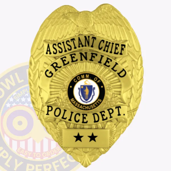 Riverbend Police Assistant Chief’s gold metal badge with eagle figure at the top, clear black text including "ASSISTANT CHIEF" and "GREENFIELD POLICE DEPT.," Massachusetts state seal centered, two black stars on a gold panel below, and safety pin attachment.