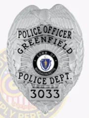 Silver metal badge for Greenfield Police Officer with an eagle emblem at the top, clear black text including "POLICE OFFICER" and "GREENFIELD POLICE DEPT.," centered Massachusetts state seal, numbered "3033," and attached by a safety pin.