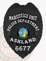 A distinctive custom metal badge in glossy black showcases "NARCOTICS UNIT" and "POLICE DEPARTMENT" at the top. The badge features an emblem of California at its center, accompanied by "ASHLAND" and badge number "6677." It is equipped with a safety pin attachment for easy application on uniforms.