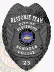A custom flex badge in black featuring the title "RESPONSE TEAM" at the top, followed by "CITY OF FLEETWOOD." The center showcases a circular emblem representing the state of Pennsylvania, surrounded by the words "SCHOOLS POLICE" in bold white text. The badge has a sleek, matte finish, emphasizing its modern design. The number "23" is displayed at the bottom, adding to the badge's official appearance. The intricate details and dark color scheme highlight its significance and authority within the community.