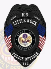 A sleek custom metal badge in black, shaped like a shield with detailed engravings. The badge features "K9" at the top, followed by "LITTLE ROCK" and "SINCE 1899" in bold white lettering. In the center, the state seal of Arkansas is displayed within a circular design, flanked by two small American flags on either side. Below the seal, "POLICE OFFICER" is clearly inscribed, along with the designation "T12" at the bottom. The matte black finish of this custom metal badge in black enhances its professional appearance, symbolizing authority and dedication in law enforcement.