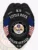 A sleek custom metal badge in black, shaped like a shield with detailed engravings. The badge features "K9" at the top, followed by "LITTLE ROCK" and "SINCE 1899" in bold white lettering. In the center, the state seal of Arkansas is displayed within a circular design, flanked by two small American flags on either side. Below the seal, "POLICE OFFICER" is clearly inscribed, along with the designation "T12" at the bottom. The matte black finish of this custom metal badge in black enhances its professional appearance, symbolizing authority and dedication in law enforcement.