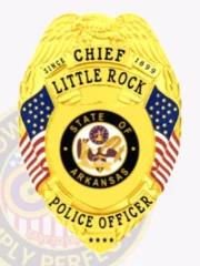 A vibrant custom metal badge gold, shaped like a shield with detailed engravings. The badge displays "CHIEF" at the top, followed by "LITTLE ROCK" and "SINCE 1899" in prominent lettering. In the center, the state seal of Arkansas is encircled by a decorative black ring, showcasing its intricate design. Flanking the seal are two small American flags, and below, "POLICE OFFICER" is clearly inscribed in bold letters. The shiny gold finish of this custom metal badge gold highlights its authority and professionalism, making it a distinguished symbol of law enforcement pride.