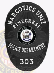 Custom black oval metal badge for Pinecrest police the narcotics unit with safety pin attachment, featuring a textured black background with radiating lines, white text reading "NARCOTICS UNIT" at the top, "PINECREST" above the State of Maine seal, "POLICE DEPARTMENT" below, and badge number "303" at the bottom.