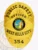 A striking custom metal badge in gold color with a safety pin attachment highlights the titles "PUBLIC SAFETY" and "OFFICER." The design includes a colorful representation of the California state seal at the center, framed by elegant gold accents.