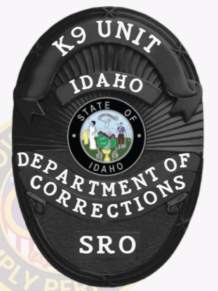 Custom metal badge in black color featuring a velcro attachment, designed for the K9 Unit of the Idaho Department of Corrections. The badge prominently displays the state emblem at the center, surrounded by the text "K9 UNIT" at the top and "DEPARTMENT OF CORRECTIONS" at the bottom. The badge is sleek and modern, with a textured background that adds depth to its design.