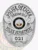 An elegant custom metal badge in silver presents a traditional oval design with detailed engravings. The words "POLICE OFFICER" are prominently displayed at the top in striking black font. The center features the Greenfield Police Department insignia, framed by "STATE OF KENTUCKY." The lower part includes "POLICE DEPARTMENT" and "021," all in clear black text. A safety pin attachment allows for convenient wear.