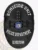 Oval black metal badge designed for Rivertown Police homicide unit with safety pin attachment, showing raised cityscape details and sunburst pattern, bold white lettering stating "HOMICIDE UNIT," "POLICE DEPARTMENT," and "RIVERTOWN," surrounding the New York state emblem at the center.