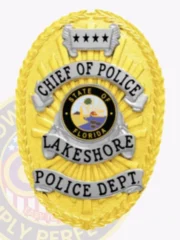 Oval gold metal badge designed for Lakeshore Police chief of police with safety pin attachment, showing a detailed laurel wreath edge in gold, radiant sunray design, silver scrolls with bold black lettering stating "CHIEF OF POLICE," "LAKESHORE," and "POLICE DEPT.," centered around the Florida state emblem.