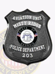Matte custom black shield metal badge for Misty Ridge police the aviation unit with safety pin attachment, showing a black shield-shaped badge with dotted texture, curved white lettering for "AVIATION UNIT" and "MISTY RIDGE," the official Georgia state seal in color, and "203" displayed below on a black panel.