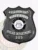 Matte custom black shield metal badge for Misty Ridge police the aviation unit with safety pin attachment, showing a black shield-shaped badge with dotted texture, curved white lettering for "AVIATION UNIT" and "MISTY RIDGE," the official Georgia state seal in color, and "203" displayed below on a black panel.