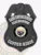 Black metal shield badge for Copper Ridge police gang enforcement, topped with a black eagle, displaying white lettering for "GANG ENFORCEMENT" and "POLICE DEPARTMENT" on upper silver panels, the Arizona state seal in black and white at the center, and "COPPER RIDGE" on the bottom banner, secured with a safety pin.