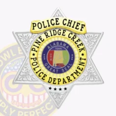 Custom silver 6-point star metal badge for pine ridge creek police chief, highlighted by gold panels including a top banner with "police chief," a circular gold ring around the multi-colored alabama great seal and department name, detailed floral patterns on silver star points, and four black stars near the bottom; equipped with a safety pin.