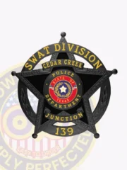 Detailed custom black metal badge with five points for Cedar Creek police SWAT Division featuring ornate engraved details on the star edges; black background contrasts with bright yellow text stating "SWAT DIVISION," "CEDAR CREEK," and "JUNCTION," encircling a vibrant Texas state seal in red and blue; the badge number "139" is shown below and includes a safety pin fastener.