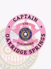 Oakridge Springs police Captain badge made of metal with a pink circle banner enclosing a five-point star; the badge displays "136" above the star, a blue state of Texas emblem in the center, and black text reading "CAPTAIN" and "OAKRIDGE SPRINGS," secured by velcro.