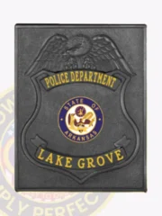 Black metal square badge for Lake Grove police featuring an eagle at the crest, yellow text banners showing "POLICE DEPARTMENT" and "LAKE GROVE," with the official Arkansas state seal in blue and gold centered within the shield, attached via safety pin.