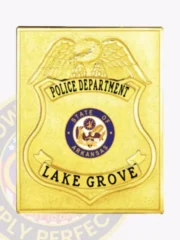 Custom-made square gold metal badge for Lake Grove police department, showcasing a gold eagle above the shield, bold black lettering on top and bottom banners reading "POLICE DEPARTMENT" and "LAKE GROVE," with a blue and gold Arkansas state seal centered, held in place by a safety pin.