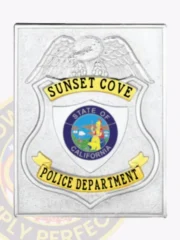 Detailed custom silver square badge with center shield for Sunset Cove Police Department, highlighted by an embossed eagle, a blue and multicolor California state seal in the center, and yellow banners with black text; equipped with a safety pin on the back.