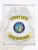 Detailed custom silver square badge with center shield for Sunset Cove Police Department, highlighted by an embossed eagle, a blue and multicolor California state seal in the center, and yellow banners with black text; equipped with a safety pin on the back.