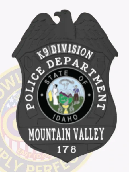 Black metal police badge shaped like a shield topped with an eagle, labeled "K9 DIVISION" and "POLICE DEPARTMENT" in white letters, showing the colorful Idaho state seal in the middle, with "MOUNTAIN VALLEY" and badge number "178" below, secured by a safety pin on the back.