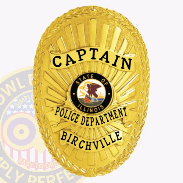 A distinctive custom metal badge in gold with safety pin attachment displays "CAPTAIN" boldly at the top in black text. Below it, "POLICE DEPARTMENT" is featured prominently, while "BIRCHVILLE" is showcased at the bottom. The central design includes the state seal of Illinois, contributing to its polished appearance.