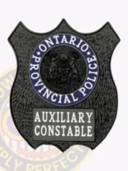 Black shield-shaped metal badge for Ontario Provincial Police Auxiliary Constable, showing the official provincial coat of arms inside a blue circle, with “Auxiliary Constable” text in white on a black plaque beneath, fastened by safety pin.