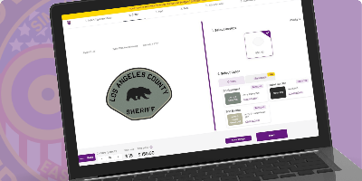 A laptop screen showcasing an online customization tool for creating custom sheriff patches. The featured patch is a sleek gray design in the shape of a shield, prominently displaying the text 'LOS ANGELES COUNTY #SHERIFF' in bold black lettering. The center of the patch features a silhouette of a bear, symbolizing the state of California. On the right side of the interface, users can select various customization options, including patch colors and sizes. This image highlights where to buy custom sheriff patches and design, create, build, and order sheriff patches through an accessible online platform.
