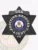 Black 6-point star flex badge customized for fugitive recovery agents in Colorado, highlighting white text encircling the colorful state seal, surrounded by embossed decorative elements, and equipped with a safety pin attachment.