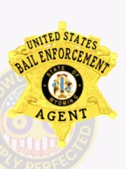 Bail enforcement agent’s custom gold metal 6 point star badge, polished to a bright shine, displaying bold black text on circular banners reading “UNITED STATES BAIL ENFORCEMENT AGENT,” with the Wyoming state seal prominently centered, attached by a safety pin.