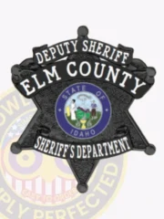 A striking black custom metal badge for deputy sheriffs features the title "DEPUTY SHERIFF ELM COUNTY" in bold lettering along the top. The center displays a round emblem representing the "STATE OF IDAHO," encircled by a blue ring. The bottom inscription reads "SHERIFF'S DEPARTMENT," all secured with a reliable safety pin attachment for easy wear.