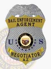 Bail enforcement agent badge in silver shield form with a raised silver eagle crest on top, gold lettering stating "Bail Enforcement Agent" and "Negotiator AZ," featuring the Arizona state seal in the center, flanked by blue letters "U" and "S," attached using a safety pin.