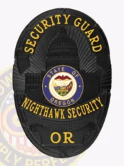A sleek custom metal badge for security guard in black, prominently displaying "SECURITY GUARD" in striking gold text at the top. The center showcases the Oregon state seal within a blue circle, accented by detailed engravings. The bottom features "NIGHTHAWK SECURITY" in elegant gold lettering, and it includes a safety pin attachment for easy fastening.