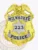 Gold metal badge for Milwaukee Police Department showcasing a raised gold eagle at the top of the shield, silver banners with bold black text MILWAUKEE and POLICE, and a silver star with the number 223 engraved in the center, designed with a safety pin attachment.