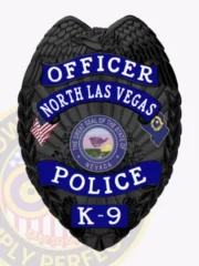North Las Vegas Police K-9 officer badge in black metal with a raised eagle on top, accented by blue reverse enamel banners stating Officer, North Las Vegas, Police, and K-9, centered around the Nevada state seal, featuring a safety pin for secure attachment.