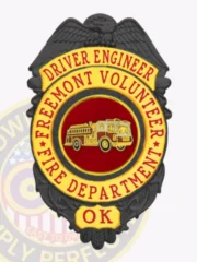 Personalized Freemont Volunteer Fire Dept. driver engineer badge in black metal with gold accents, bold red text surrounding a red circle showcasing a gold fire truck emblem, complete with safety pin for attachment.