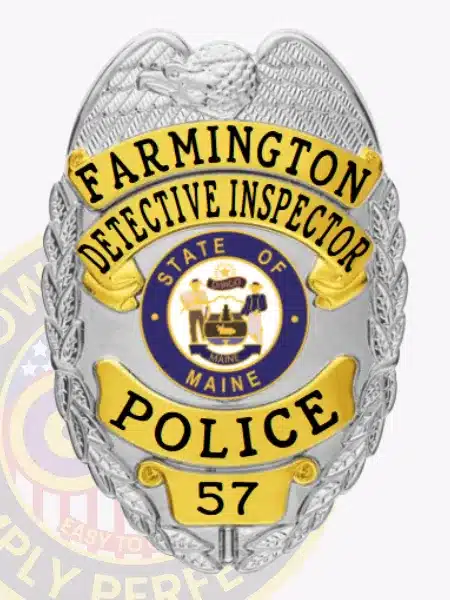 Silver custom metal badge with gold panels for Farmington Police Detective Inspector, decorated with an eagle symbol at the top, clear black embossed lettering "FARMINGTON DETECTIVE INSPECTOR POLICE 57," and a State of Maine insignia at center, attached using a safety pin.