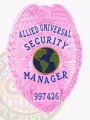 Allied Universal Security Manager badge in custom BCAM pink color with detailed eagle at the top, blue text panels, a globe emblem in the center, and safety pin attachment on the back.