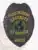 Black metal security badge custom-made for Allied Universal K9 officers, showing a detailed eagle design at the top, a central globe icon in blue and green, bold yellow lettering for "Security K9 Officer," and a safety pin fastener for secure attachment.