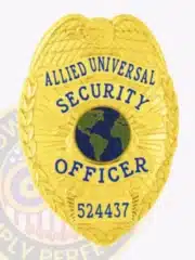 Detailed image of a custom gold eagle top metal badge for Allied Universal, highlighting the textured eagle wings, globe symbol in blue and green, officer title in blue letters, and identification number 524437, equipped with a safety pin attachment.
