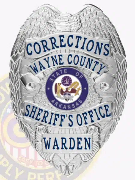 Detailed photo of a silver law enforcement badge for Wayne County Corrections, showing a raised eagle design on top, silver ribbons with blue text stating "Corrections Wayne County Sheriff's Office Warden," and the Arkansas state emblem in the center.