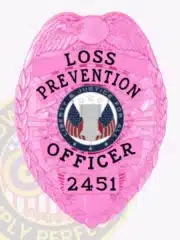 Detailed image of a bright pink Lost Prevention Officer badge made of metal, topped with an eagle design, black lettering "LOSS PREVENTION OFFICER 2451," and a round emblem in the center displaying patriotic symbols and justice-themed wording, designed with a safety pin for secure fastening.