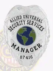 Detailed image of a custom silver eagle top metal badge for Allied Universal, highlighting the textured eagle wings, globe symbol in the center, manager title in bold black letters, and identification number 87416, equipped with a safety pin attachment.
