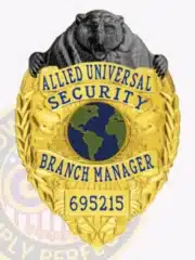Gold metal security badge with custom black bear top for Allied Universal Branch Manager, featuring a globe image in the center and secured by a safety pin on the back.