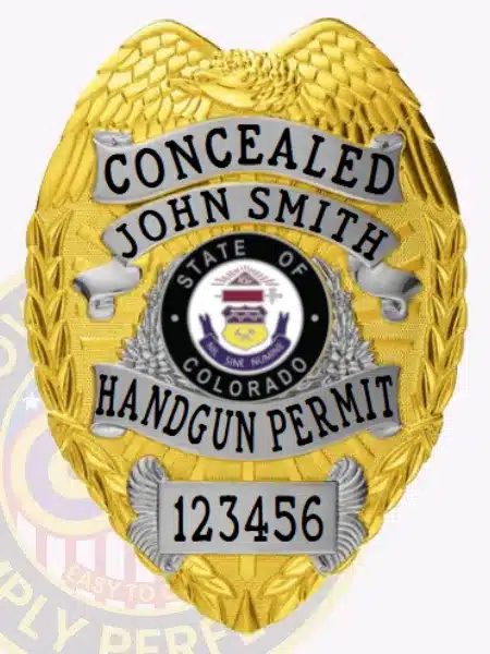 Gold concealed handgun permit badge with detailed silver panels including banners for "CONCEALED," the name "John Smith," and "HANDGUN PERMIT," displaying the official Colorado state seal in the center, a serial number 123456 on a silver plate at the bottom, secured with a safety pin.