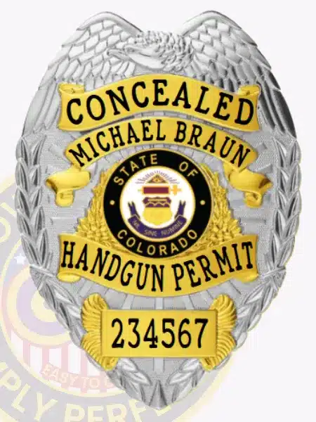 Detailed silver and gold metal concealed handgun permit badge, personalized with the name Michael Braun, showing gold accents on the text panels including "CONCEALED" and "HANDGUN PERMIT," the Colorado state emblem in the middle, a serial number 234567 in gold at the bottom, and a safety pin attachment for secure wear.