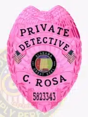Bright pink metal badge for Alabama private detective C. Rosa, with an eagle design at the top, clear black lettering including “PRIVATE DETECTIVE” and the badge number “5823343,” centered around the Alabama Great Seal and two American flags, equipped with a safety pin.