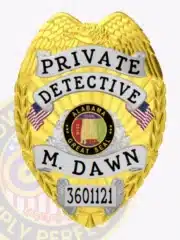 Close-up image of a gold metal badge with silver panels for an Alabama private detective, featuring an eagle emblem at the top, clear black text with the name and title, the Alabama state seal in the middle flanked by two American flags, and a metal safety pin clasp.