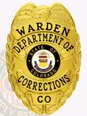Custom gold metal badge with an eagle at the top, featuring black lettering for the Warden of the Department of Corrections, Colorado. The badge's center displays the official state seal, and it has a safety pin attachment.