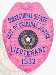 Close-up image of a custom BCAM pink metal badge for the Department of Criminal Justice, featuring an eagle at the top, with blue text on pink panels reading "Correctional Officer Dept. of Criminal Justice Lieutenant," centered around the State of Texas seal, and displaying badge number 1532 with a safety pin attachment.